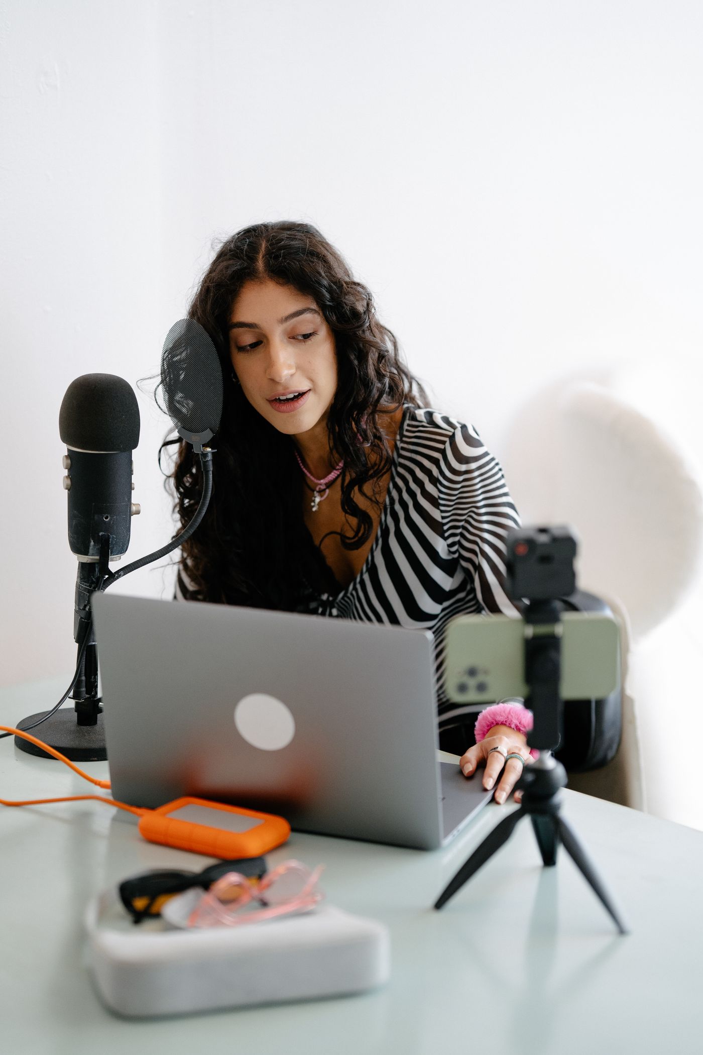 A woman recording at her desk with a microphone and laptop.