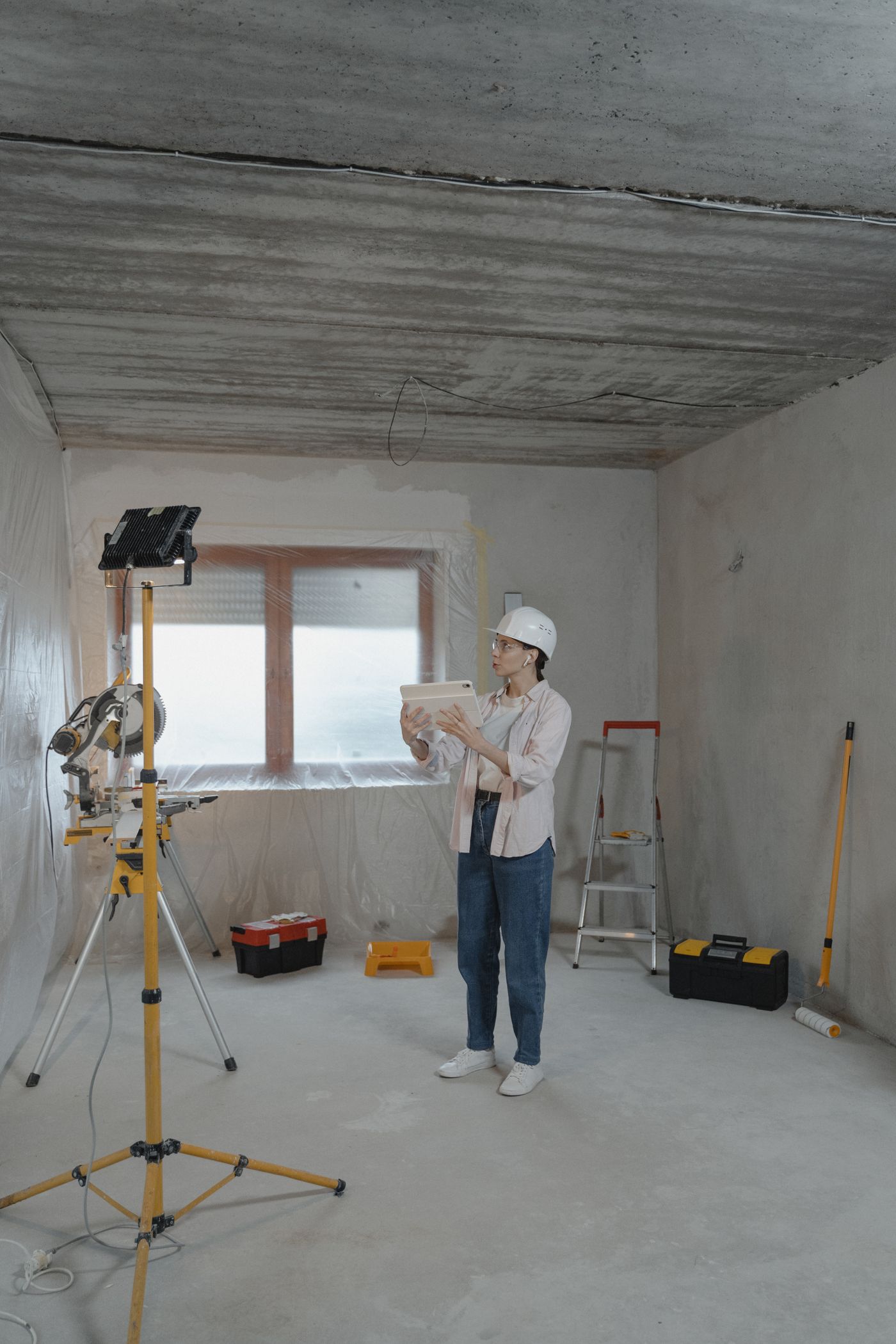 A woman in a hard hat checking a tablet on a home renovation site.