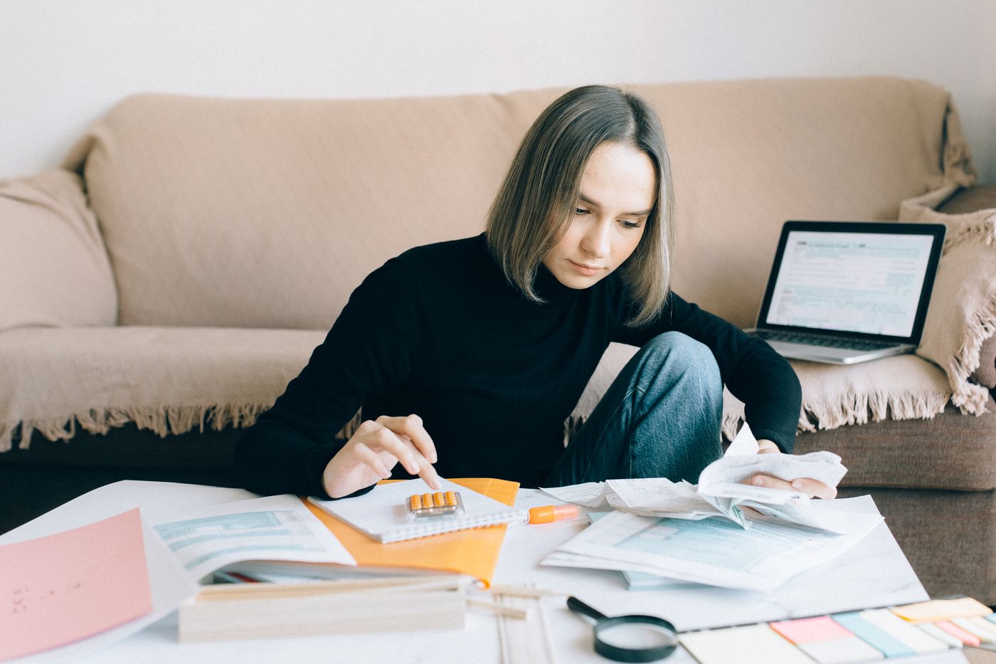 A woman working through her finances with papers and a laptop at home.