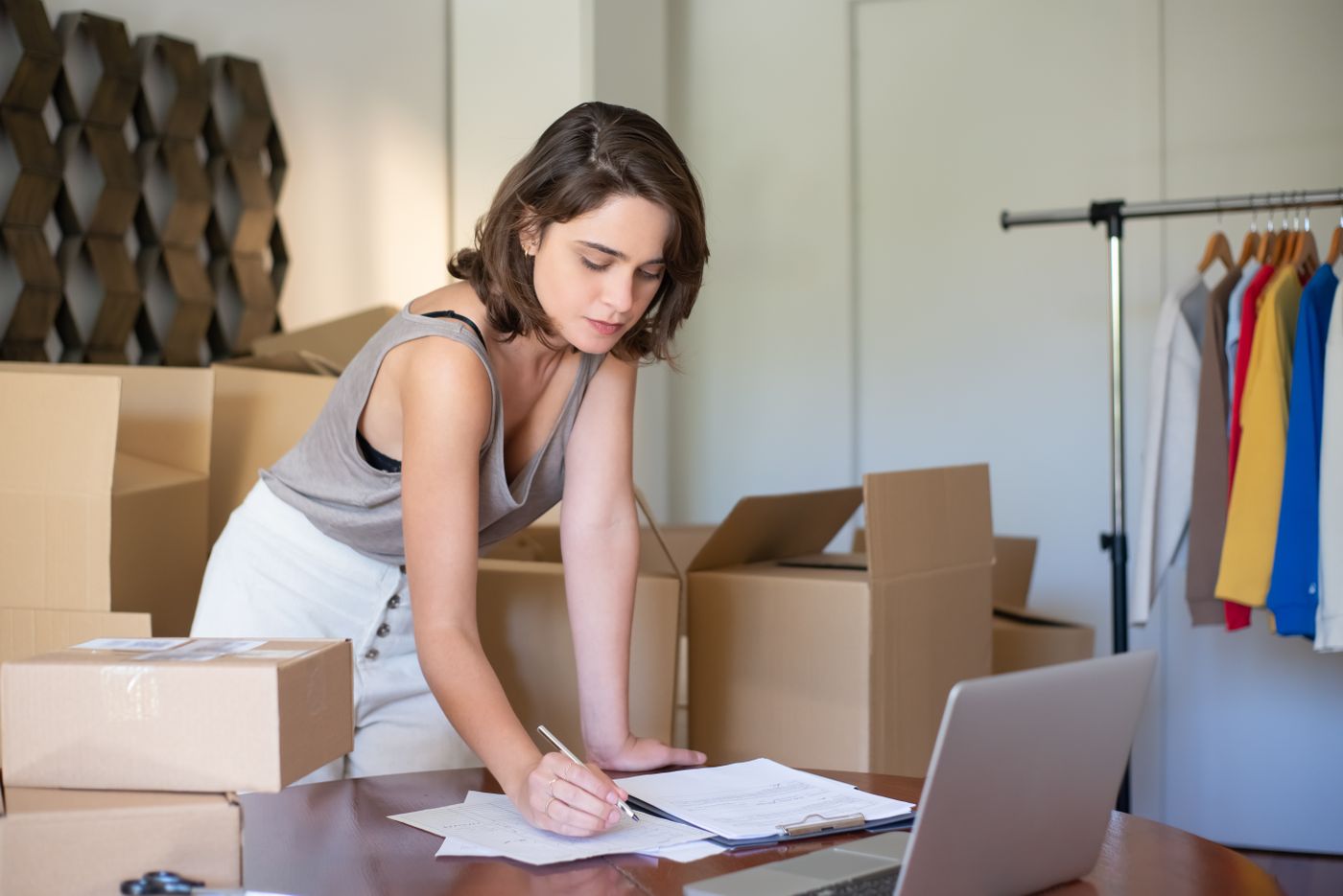A woman running her online clothing business from a home office, with a laptop and packed boxes.
